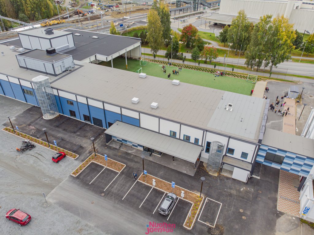 Ulkokuva Sirkkalan liikkumiskeskuksesta. Yläviistosta otetusta kuvasta näkyy pysäköintialue sisäänkäynnin puolella ja takana oleva tekonurmen päällysteinen piha-alue. Käytävä yhdistää keskuksen viereiseen koulurakennukseen.